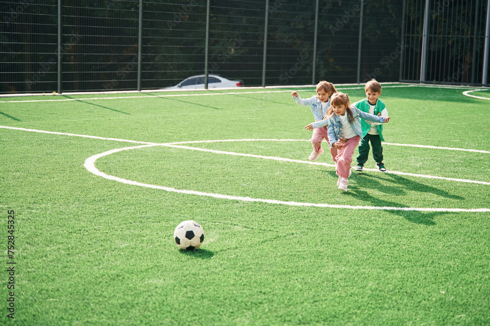 Obraz premium Running with ball. Kids are having fun on the green soccer field together