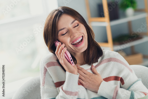 Photo of positive overjoyed lady sit chair hand touch chest speak telephone laughing pastime flat indoors