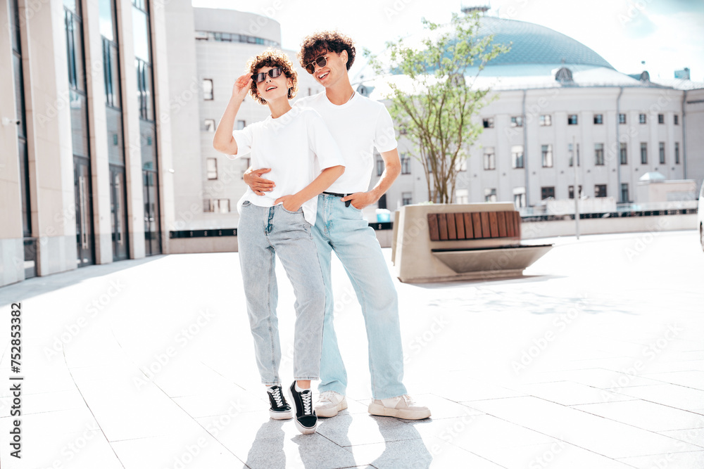 Young smiling beautiful woman and her handsome boyfriend in casual summer white t-shirt and jeans clothes. Happy cheerful family. Female having fun. Couple posing in street at sunny day, sunglasses