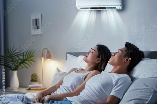 A couple relaxing in bed under an air conditioner, enjoying the cool air in a cozy, dimly lit bedroom