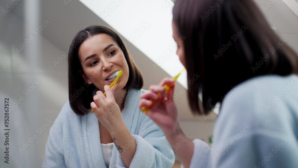 A woman is brushing her teeth, smiling at her reflection in the mirror A woman is brushing her teeth, smiling at her reflection in the mirror
