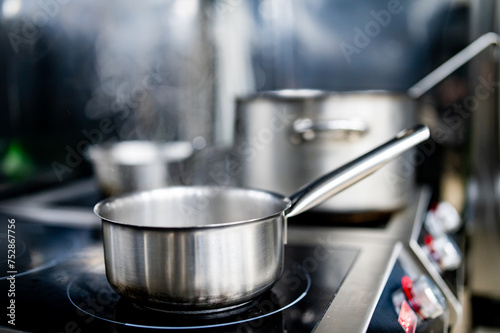 A stainless steel frying pan on a modern stove, with another pot in the background, in a kitchen with natural lighting.