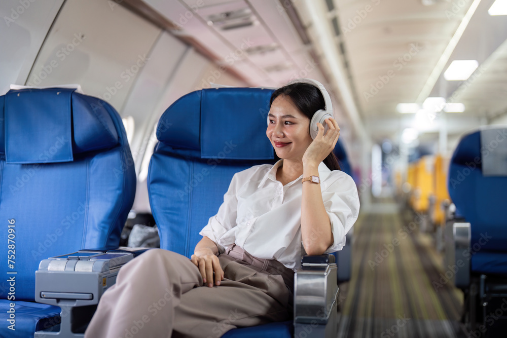 Asian young woman wearing headphone listen to music at first class on airplane during flight, Traveling and Business concept