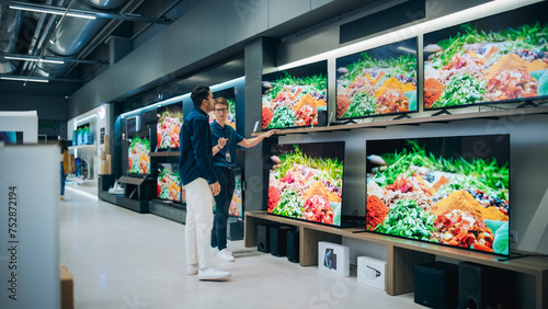 Young Multiethnic Customer Advising with Retail Home Electronics Store Salesperson. Stylish Man is Interested in Buying a Flat-Screen TV. Client Shopping for a New Television Set in Modern Shop photo