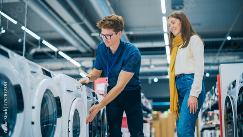 Portrait of a Retail Electronics Shop Consultant Assisting Young Female Customer in Selecting a Washing Machine For Her Home. Beautiful Female Evaluating Modern Laundry Solutions