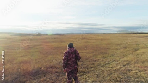 A hunter with a gun walks across a field in autumn
