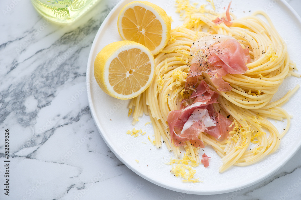 Plate of spaghetti with prosciutto and lemon zest, horizontal shot on a white marble background, middle closeup