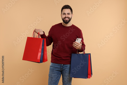 Smiling man with many paper shopping bags and smartphone on beige background