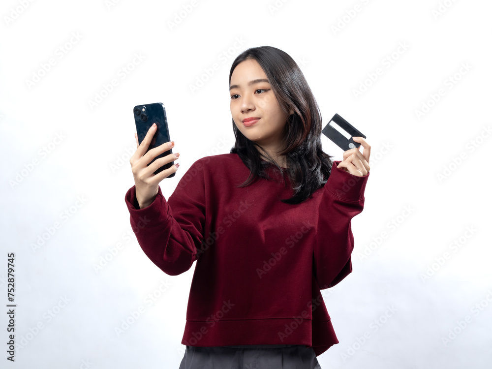 Smart Asian woman with phone and credit card ready for online shopping, in a red sweater, white background Smart Asian woman with phone and credit card ready for online shopping, in a red sweater, white background
