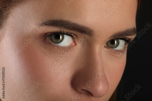 Evil eye. Young woman with scary eyes on black background, closeup