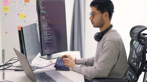 A male software developer studies his code intently on dual monitors in a well-lit workspace of a dynamic tech environment.