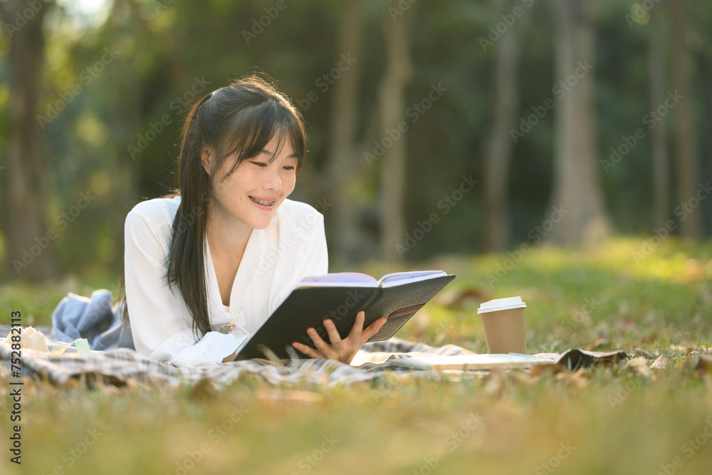 Peaceful young Asian woman lying on picnic blanket and reading her reading her favorite book Peaceful young Asian woman lying on picnic blanket and reading her reading her favorite book