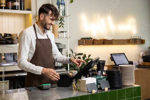 Man waiter working in coffee shop using terminal while standing at counter photo