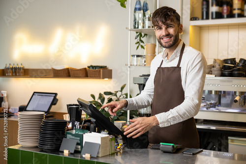 Waiter man working in coffee shop using terminal for checking orders standing at counter