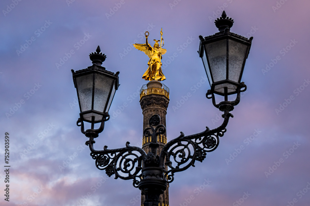 Berlin Victory Column, Siegessäule, stands resplendent in the warm glow of the sun, its golden hue illuminated by the evening light, while lanterns frame this iconic monument, adding to its beauty.