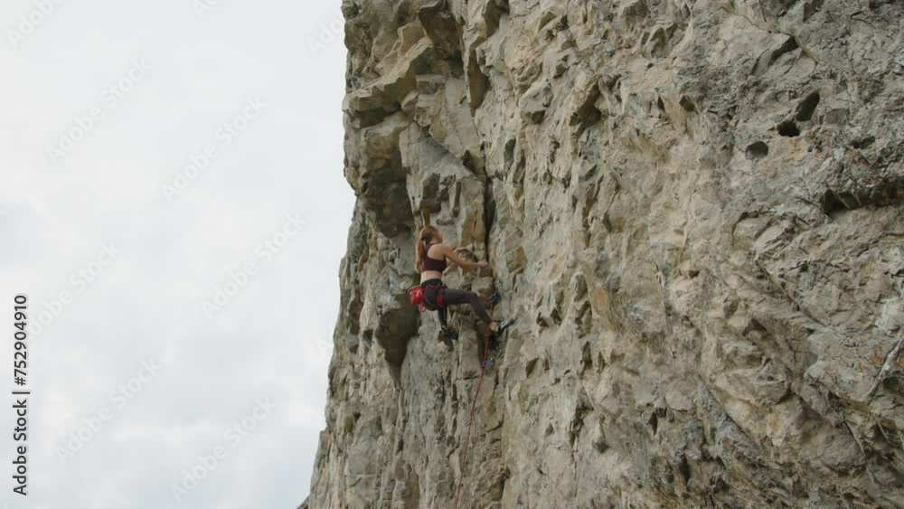 Wide shot of young female climber going up rocky cliff and using chalk for hands during climb