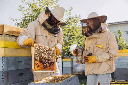 International team of happy beekeepers, man takes out a wooden frame from a beehive and a woman holds smoker © anatoliycherkas