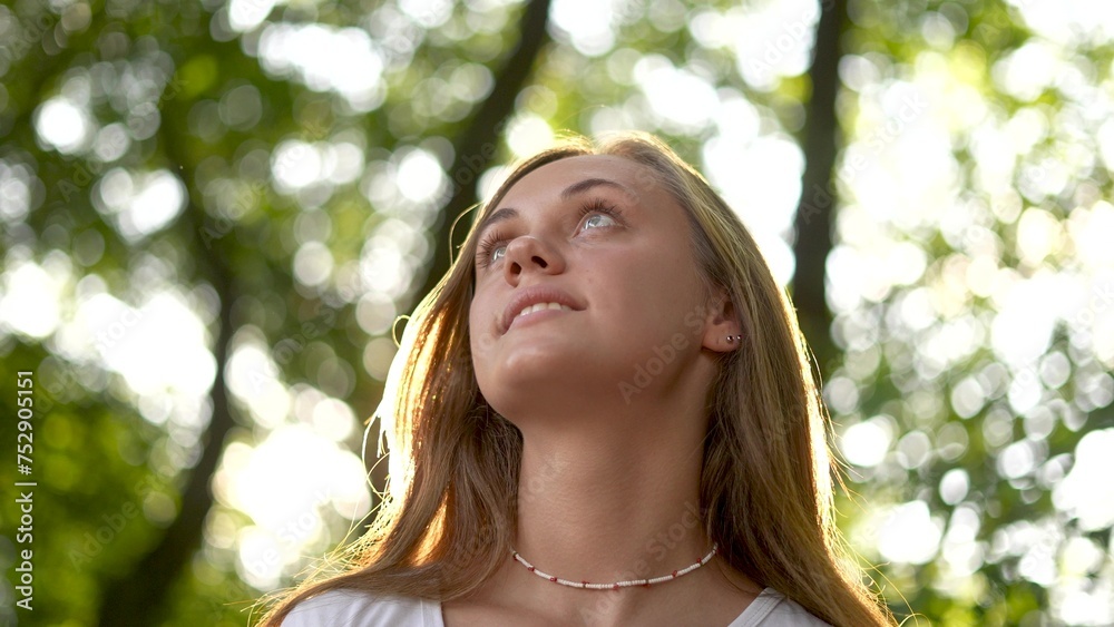 Naklejka premium beautiful girl smiling. inner beauty and love for lifestyle nature concept. beautiful woman stands in a park outdoors in a white T-shirt and smiles, face close-up, sun glare on the background
