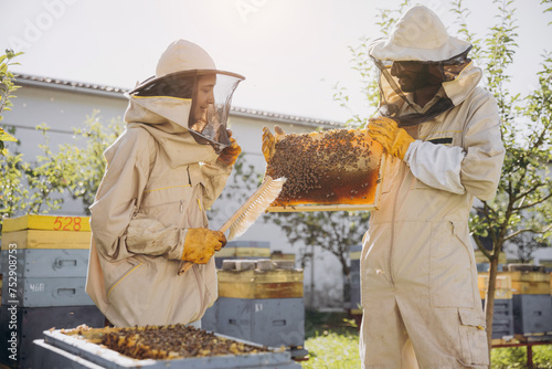 Couple of beekeepers working with a wooden frame near a beehive in beekeeping © anatoliycherkas