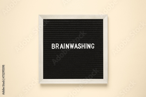 The word brainwashing on black letter board over isolated beige background.