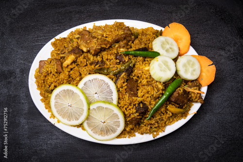 Beef Yakhni biryani rice pulao with cucumber, lime slice and carrot served in dish isolated on dark background top view indian spices, bangladeshi and pakistani food photo