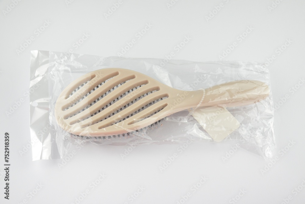 New beige oval hairbrush with bristles and a white tag in a transparent plastic package on a white background New beige oval hairbrush with bristles and a white tag in a transparent plastic package on a white background