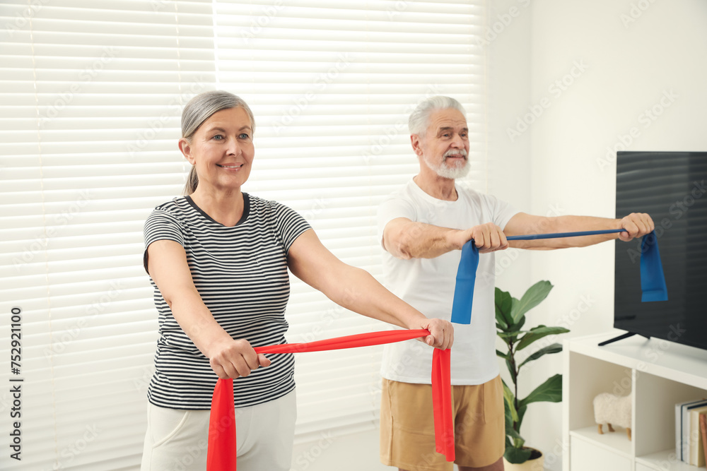 Obraz premium Senior couple doing exercise with fitness elastic bands at home, selective focus