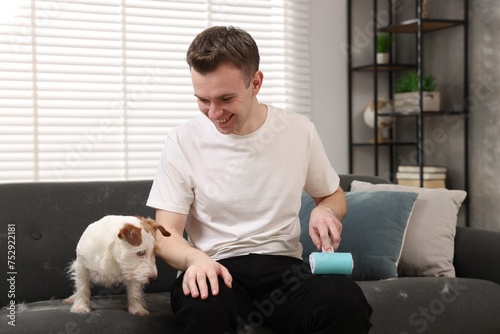 Pet shedding. Smiling man with lint roller removing dog's hair from pants at home