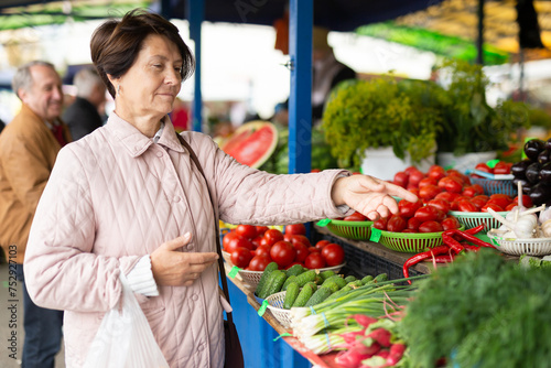 Elderly woman buys vegetables at an open air market photo
