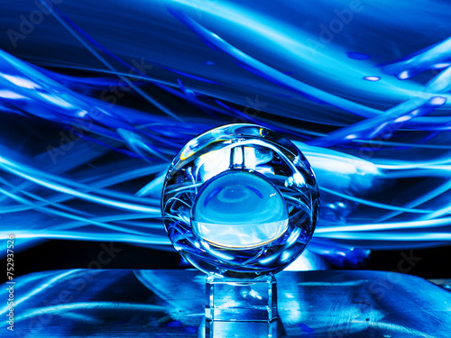 Glass ball on a metal surface, dark background with blue dynamic ight painting. Fortune telling or forecast concept. photo