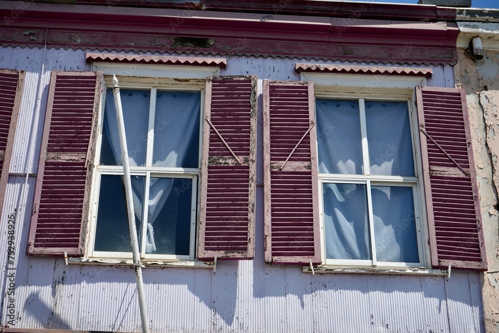 Rustic mauve shuttered windows on a corrugated metal building in the sunshine. Rustic mauve shuttered windows on a corrugated metal building in the sunshine.