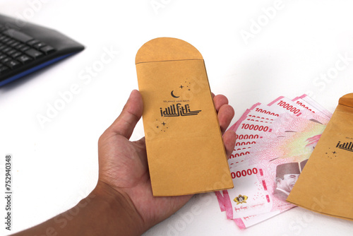 Hand holding a THR envelope filled with Indonesian Rupiah banknotes. THR or Tunjangan Hari Raya is a holiday allowance or bonus traditionally given to employees and those in need near during Ramadan photo