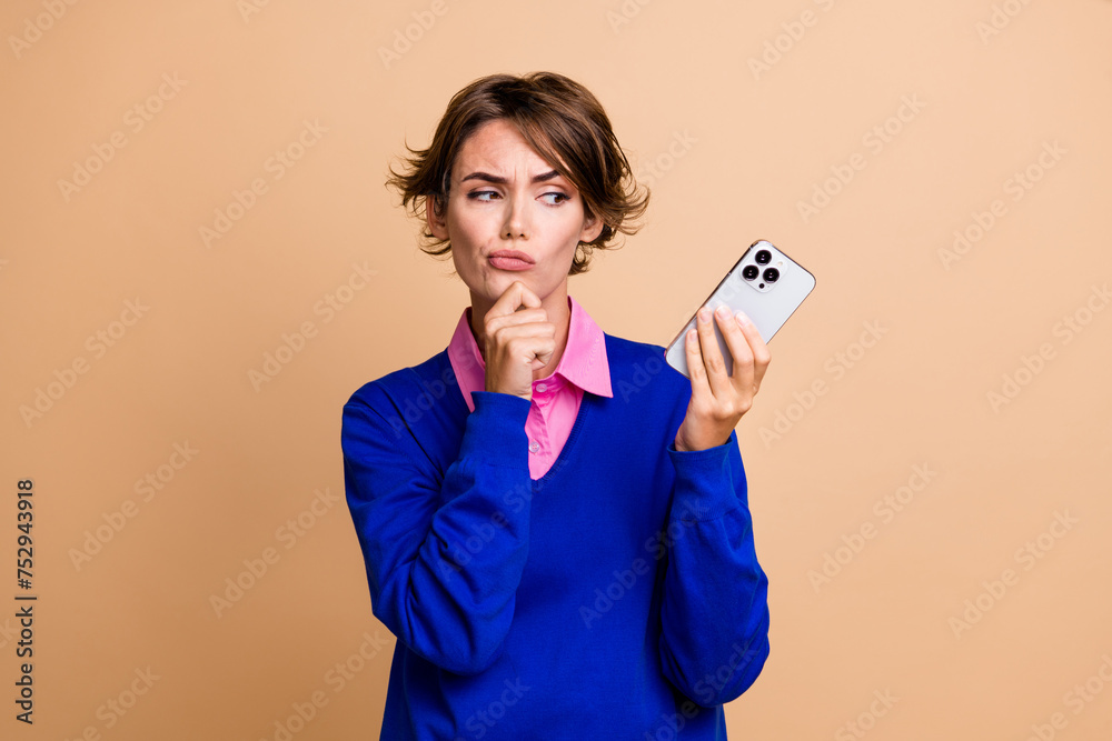 Photo of minded pensive person hand touch chin look smart phone brainstrom decide isolated on beige color background Photo of minded pensive person hand touch chin look smart phone brainstrom decide isolated on beige color background
