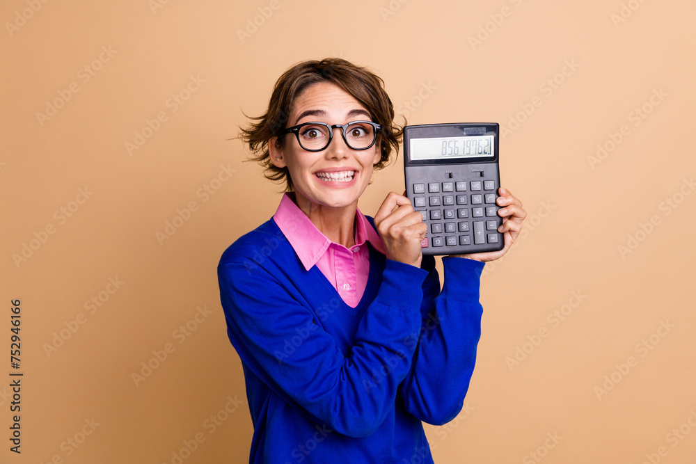 Photo portrait of attractive young woman show hold excited calculator dressed stylish blue clothes isolated on beige color background Photo portrait of attractive young woman show hold excited calculator dressed stylish blue clothes isolated on beige color background