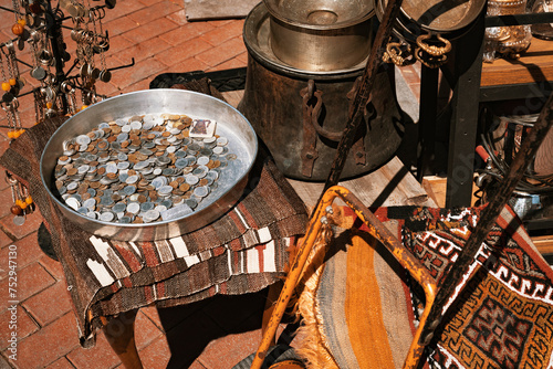 Obraz na plátně Vintage coins in a metal tray, rusty old cauldron and pots, key chains, rug and other goods in a shop at bazaar