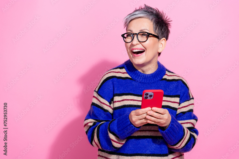 Fototapeta premium Photo of attractive pensioner woman hold device look empty space dressed stylish blue striped clothes isolated on pink color background