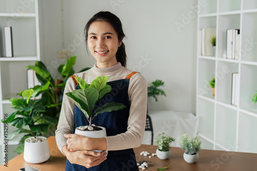 Portrait of a smiling young woman holding potted plant in the house and taking care of the greenery of the house