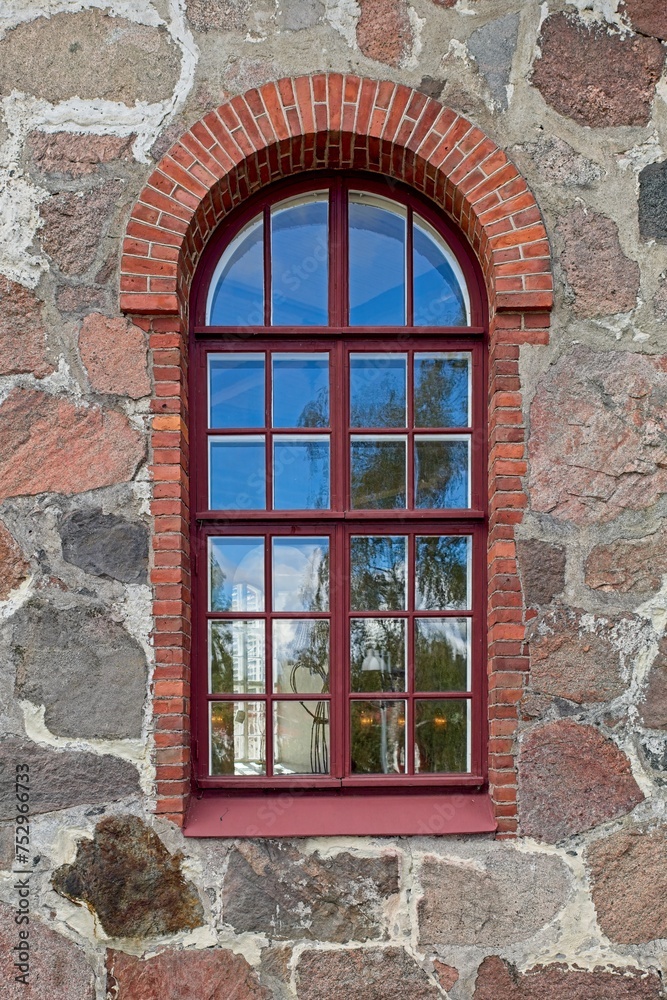 Fototapeta premium Window with red frame with red brick arch on a old stone building.