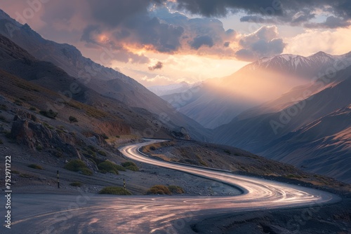 Curved mountain road at dusk with sunlight piercing through clouds