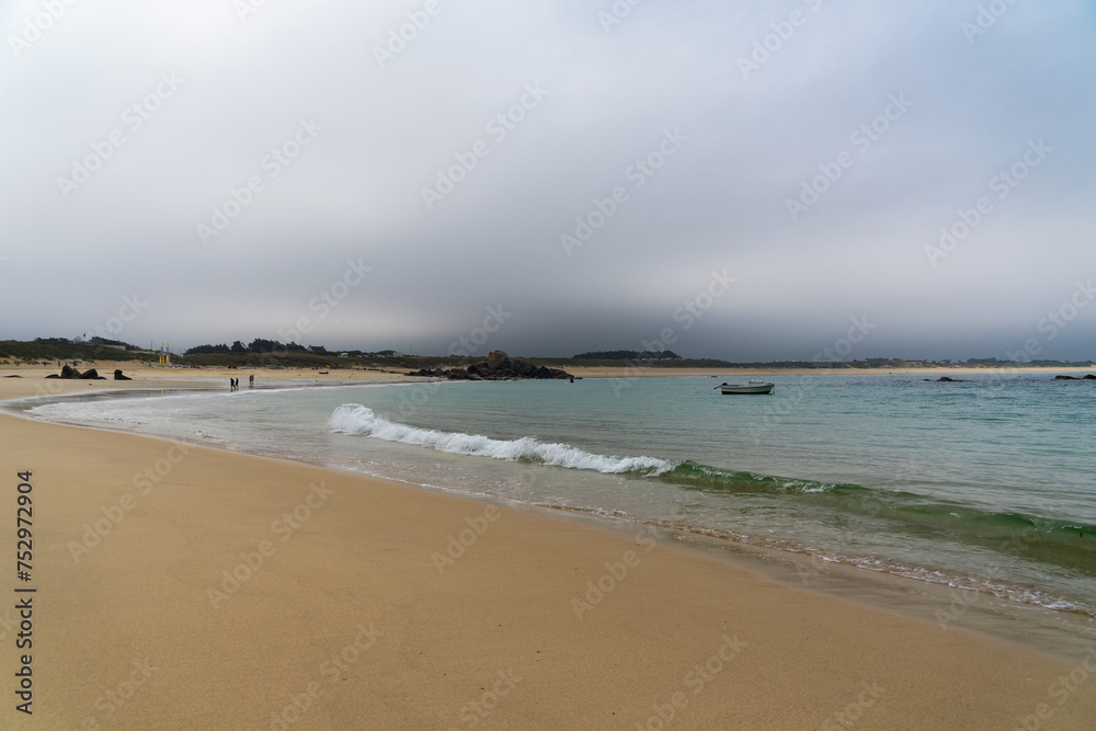 Plage de sable fin et eaux vert émeraude sous un ciel menaçant en Bretagne