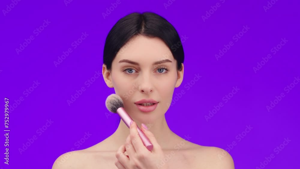 Close-up portrait of an attractive beautiful young topless woman standing isolated on a purple background with a makeup brush. Concept of cosmetology, cosmetic care products. Close-up portrait of an attractive beautiful young topless woman standing isolated on a purple background with a makeup brush. Concept of cosmetology, cosmetic care products.