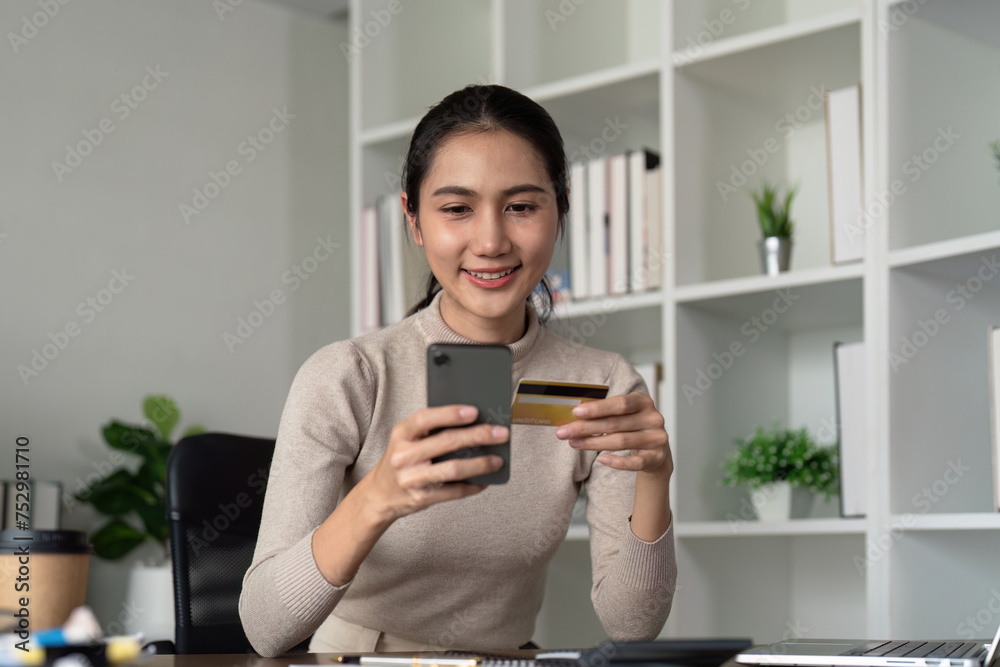 Happy young asian woman holding credit card using mobile payment at home. Smiling Female customer shopping making purchase on smartphone receiving cash back concept