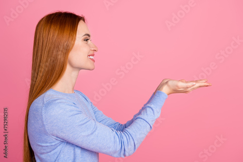 Side profile photo of positive optimistic woman dressed blue shirt look at object on arms empty space isolated on pink color background
