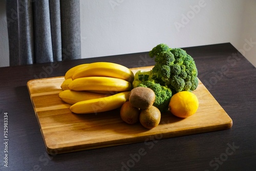 Warzywa i owoce leżą na desce do krojenia. Brokuł, banany, kiwi i cytryna.