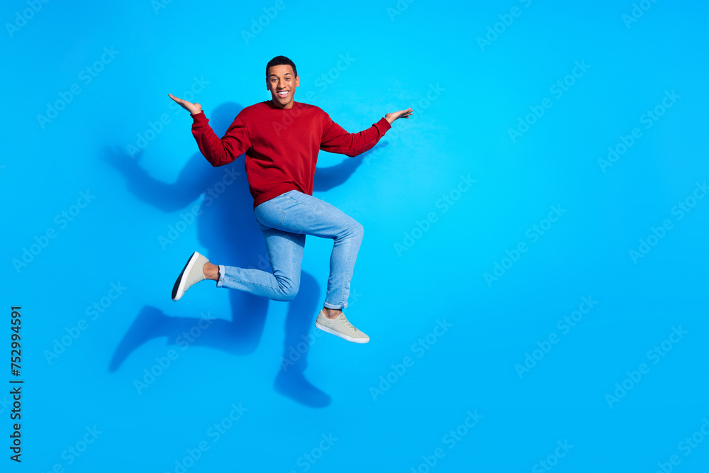 Fototapeta premium Full size profile photo of sporty carefree person jump run arms hold empty space isolated on blue color background