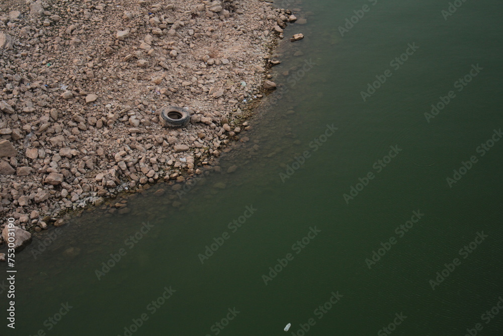 Environmental Degradation: Pollution in Tranquil Waters. juxtaposition of a lake with a littered pebbly shore, highlighting environmental challenges. Environmental Degradation: Pollution in Tranquil Waters. juxtaposition of a lake with a littered pebbly shore, highlighting environmental challenges.
