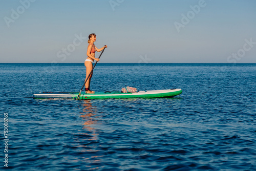 Woman paddling on stand up paddle board, sea on sunny summer day. Relaxing on blue ocean