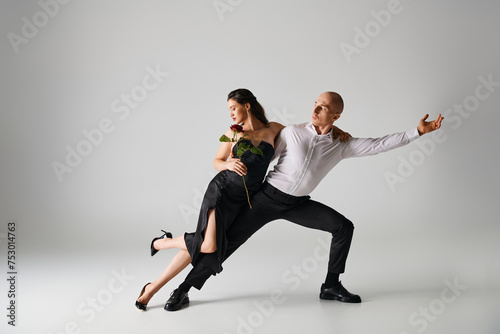 dance motion of young couple, brunette woman holding red rose and man in formal attire in studio