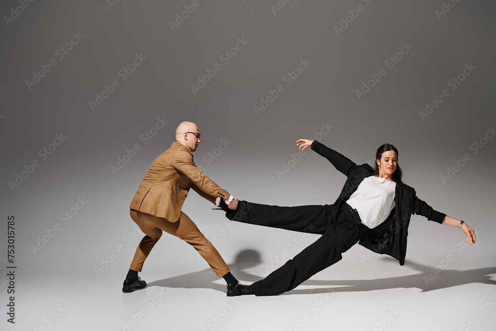 Dynamic dancers in business attire performing a balancing act in a studio with grey background Dynamic dancers in business attire performing a balancing act in a studio with grey background