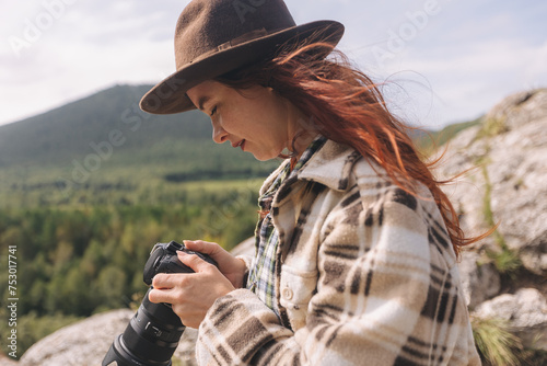 A young female tourist in a hat takes pictures of the mountains. Hiking on the Shaman's path, Khakassia, Russia photo